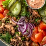 A vibrant burger bowl filled with ground beef, lettuce, tomatoes, and cheese.